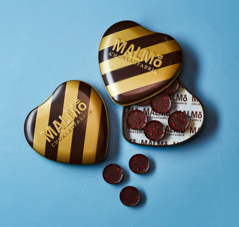 Brun och guldigt randig plåtask formas som ett hjärta fyllt med runda chokladbitar med strösslade hallon på. 